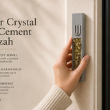 Hand holding a Modern Golden Amber Crystal Inlay Gray Cement Mezuzah case with a raised silver-tone Shin and warm golden amber crystal and glass pieces, showing the contrast between the cool gray cement body and rich honey, bronze, and amber-toned inlay