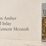 Modern gray cement mezuzah displayed upright in a minimalist setting with a raised silver-tone Shin and vertical golden amber crystal and glass inlay, highlighting warm honey, bronze, and gold reflections against the cool neutral cement surface