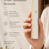 Person holding a white and gold aluminum mezuzah showing its sleek design with natural light and generous space.