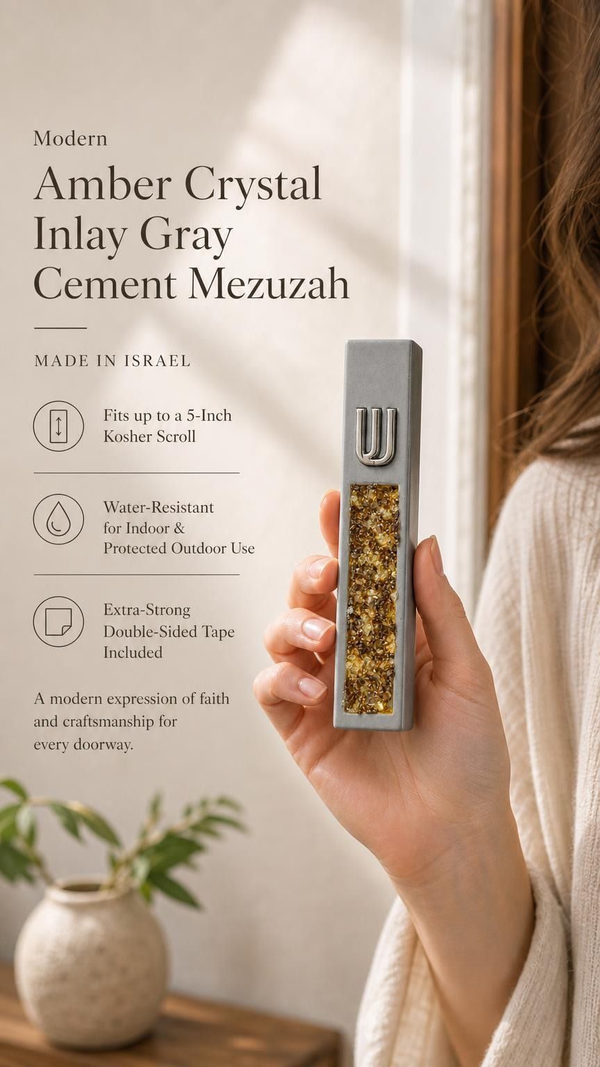 Handheld modern gray cement mezuzah case with a raised silver-tone Shin and golden amber crystal and glass inlay, presented beside product details in a soft neutral interior to show the slim case profile, natural-looking warm color variation, and reflective finish