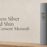 Minimalist gray cement mezuzah case featuring a raised silver Hebrew letter Shin on a soft, neutral stone-colored background