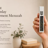 Hand holding a Modern Iridescent Crystal Inlay White Cement Mezuzah case with a raised silver-tone Shin and reflective crystal and glass inlay showing pearl, charcoal, bronze, blue-gray, green, and iridescent tones in a warm contemporary interior