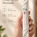 Person holding a white acrylic mezuzah case featuring sculpted Jerusalem wall patterns and a central silver Hebrew Shin letter.