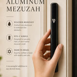 Modern black aluminum mezuzah case with Shin detail, designed for outdoor doorways with secure screw-in cap and water resistance.