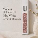 Modern white cement mezuzah displayed against a soft minimalist background with a raised silver-tone Shin and decorative pink crystal and glass inlay, showing blush, rose, pale pink, and reflective tones in a clean contemporary Judaica design