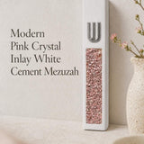 Modern white cement mezuzah displayed against a soft minimalist background with a raised silver-tone Shin and decorative pink crystal and glass inlay, showing blush, rose, pale pink, and reflective tones in a clean contemporary Judaica design