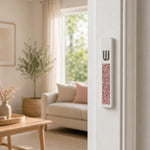 Modern Pink Crystal Inlay White Cement Mezuzah mounted vertically on a light residential doorpost, showing the raised silver-tone Shin and sparkling blush and rose crystal inlay in a bright contemporary home or living room doorway
