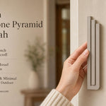 Person holding the exact modern sandstone pyramid mezuzah, showing its architectural form and warm greige aluminum finish, with editorial text beside
