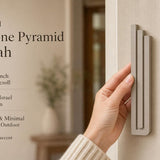 Person holding the exact modern sandstone pyramid mezuzah, showing its architectural form and warm greige aluminum finish, with editorial text beside