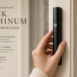 Hand-held view of the modern waterproof black aluminum outdoor mezuzah, showcasing its slim black silhouette with a raised silver Shin