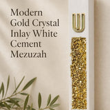 Modern Gold Crystal Inlay White Cement Mezuzah shown beside product details, featuring a raised gold Shin and shimmering gold crystal and glass inlay on a slim contemporary white cement case designed as modern Israeli Judaica for the doorway