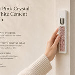 Handheld modern white cement mezuzah case featuring a raised silver-tone Shin and pink crystal and glass inlay, shown beside product information in a warm neutral home setting to highlight its slim profile, soft rose color palette, and contemporary styling