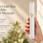 A hand holding a white mezuzah cover with a gold-tone crowned Shin and clipped corner design.