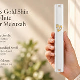 A hand holding a white mezuzah cover with a gold-tone crowned Shin and clipped corner design.