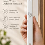 Close up of a hand holding an opaque white mezuzah with a silver Hebrew Shin designed for outdoor doorposts.