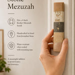 A person holding a natural Jerusalem stone mezuzah case with gold Hebrew lettering, captured in warm, soft natural light.