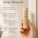 Person holding Jerusalem stone mezuzah horizontally, showcasing its texture and design with natural light and detailed focus.