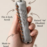 Person holding pewter mezuzah delicately with a support hand, showcasing artisanal craftsmanship and religious symbolism in a minimalist style.