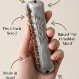 Person holding pewter mezuzah delicately with a support hand, showcasing artisanal craftsmanship and religious symbolism in a minimalist style.