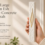 Hand holding an extra large golden Esh mezuzah made of textured white concrete for a doorway.