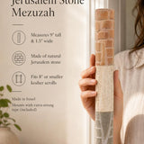 Close up of a hand holding an extra large layered Jerusalem stone mezuzah case with natural beige textures.