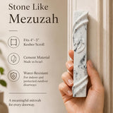 Person holding the exact stone-like mezuzah in a natural pose, emphasizing size and material, for a premium store presentation.