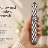 A person holding a premium silver-toned spiral stainless steel mezuzah featuring ornate end caps and a traditional Shin letter.