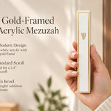 Handheld Lumen mezuzah featuring a gold frame and white acrylic finish in a styled editorial setting.