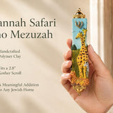 Savannah Safari Fimo Mezuzah mezuzah cover held upright in one hand, showing a pale blue Fimo body with tall yellow giraffes, a zebra, spotted animals, green scenery and a gold-colored Hebrew Shin beneath decorative brass fittings beside the product name and illustrated design features in a wide social-sharing graphic for decorative Jewish home Judaica