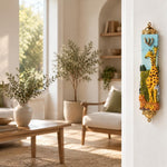 Savannah Safari Fimo Mezuzah mounted vertically on a pale home doorpost, with a pale blue Fimo body with tall yellow giraffes, a zebra, spotted animals, green scenery and a gold-colored Hebrew Shin beneath decorative brass fittings creating a distinctive mezuzah cover that brings its Jewish design and decorative detail into the doorway