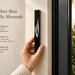 Large black acrylic mezuzah cover mounted vertically on a light-colored front doorpost, showing its slim profile and contrasting silver Shin