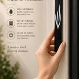 A person holding a sleek black acrylic mezuzah case featuring a prominent silver Shin letter designed for outdoor entryways