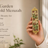 Secret Garden 24K gold-plated mezuzah case held in a woman’s hand, featuring colorful hand-painted floral enamel, green leaves, jeweled flowers, Swarovski crystals, and ornate gold detailing. This elegant Jewish Judaica mezuzah case fits a 4-inch kosher mezuzah scroll and makes a meaningful wedding, housewarming, or new home gift