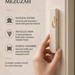hand holds the Small Modern Cream Jerusalem Stone Mezuzah beside a light doorpost, showing its narrow stone body and gold Shin alongside graphic callouts about the natural stone and scroll chamber