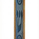 Stone and glass mezuzah with blue frosted glass Shin and swirl design, mounted on a white studio surface with soft reflection.