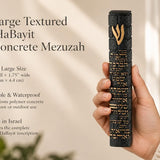 A hand holding a Extra Large Textured Birkat HaBayit Black Concrete Mezuzah made in Israel with gold Hebrew lettering
