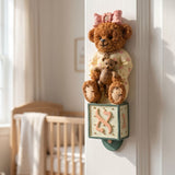 Hand-painted Teddy Aleph Bear Mezuzah case in soft cream, pink, brown, and green tones, mounted inside a doorway in a nursery or child's room.