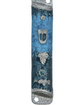 Pewter mezuzah with enamel paint, featuring a floating leaf on a blue background, displayed on a white studio surface with soft reflection.