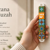 A hand holds the colorful ceramic Toscana Mezuzah case featuring orange, green, and blue floral motifs with a central Hebrew Shin.