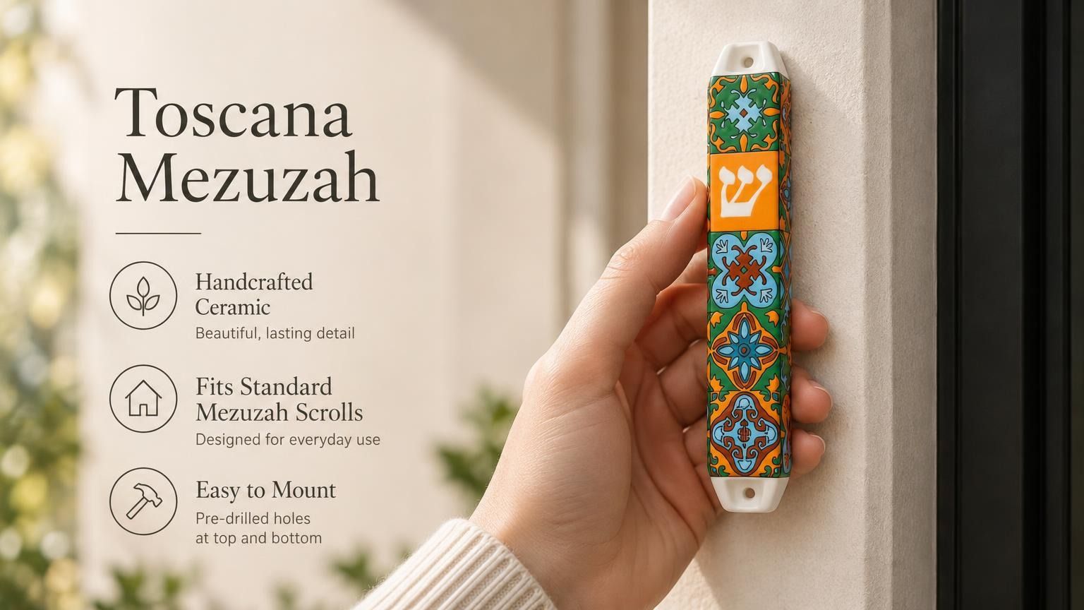 A hand holds the colorful ceramic Toscana Mezuzah case featuring orange, green, and blue floral motifs with a central Hebrew Shin.