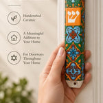 A person holding the colorful floral Toscana ceramic mezuzah with orange, green, and blue tile-like motifs and a white Shin.