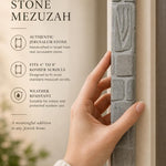 Hand-held view of a handcrafted Jerusalem stone mezuzah case with carved Shin, natural grey tone, on a neutral background.