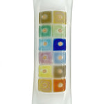 Contemporary glass mezuzah with fused-glass checkerboard pattern, 4.5 inches tall, mounted on a polished white studio surface with light reflection.