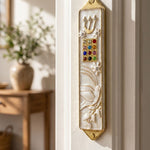 Twelve Jewels Dove Pearl pewter mezuzah case with gold Shin, jeweled Choshen-style panel, white dove, flowers, and pearl enamel, mounted on a door frame in a modern interior design style.