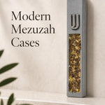 Close product view of a unique gray cement mezuzah case with a raised silver-tone Shin and long decorative inlay filled with golden amber, honey, bronze, and warm crystal and glass tones, styled against a clean contemporary background on a stone surface