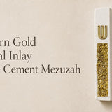 Unique modern white cement mezuzah displayed against a soft minimalist interior background, featuring a raised gold Shin above a long recessed panel of gold crystal and glass inlay with champagne, metallic gold, and reflective highlights