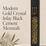 Close view of a unique modern black cement mezuzah case featuring a raised gold Shin above a long inset panel filled with reflective golden crystal and glass pieces, styled against a simple neutral background for a bold contemporary Judaica look
