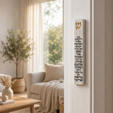 Close view of a unique white cement Birkat HaBayit mezuzah case with a raised gold Shin and complete Hebrew home-blessing inscription running vertically down the front, styled against a clean neutral interior background