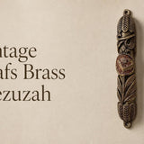 Vintage Leafs brass mezuzah case mounted on a neutral wall, featuring an aged antique brass finish, deeply sculpted leaves and botanical details, and a raised Hebrew Shin medallion at the center. This traditional brass mezuzah case brings warm vintage Judaica character to a Jewish home, entryway, or interior doorway