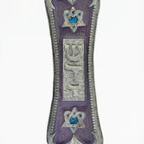 Elegant pewter mezuzah with violet pearlescent face, framed Hebrew letter Shin, Star of David symbols, on a white studio background with soft reflection.